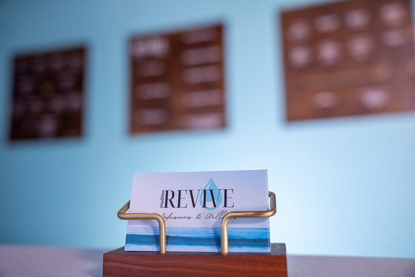 IV-infusions-nad-therapy-nutrients-consultations-customized-wellness-solutions Revive Infusions & Wellness business card in a wooden holder on the front desk of the reception and waiting area in Roseburg, Oregon, ready for new patient inquiries about IV therapy, peptide treatments, hormone optimization, and wellness programs.